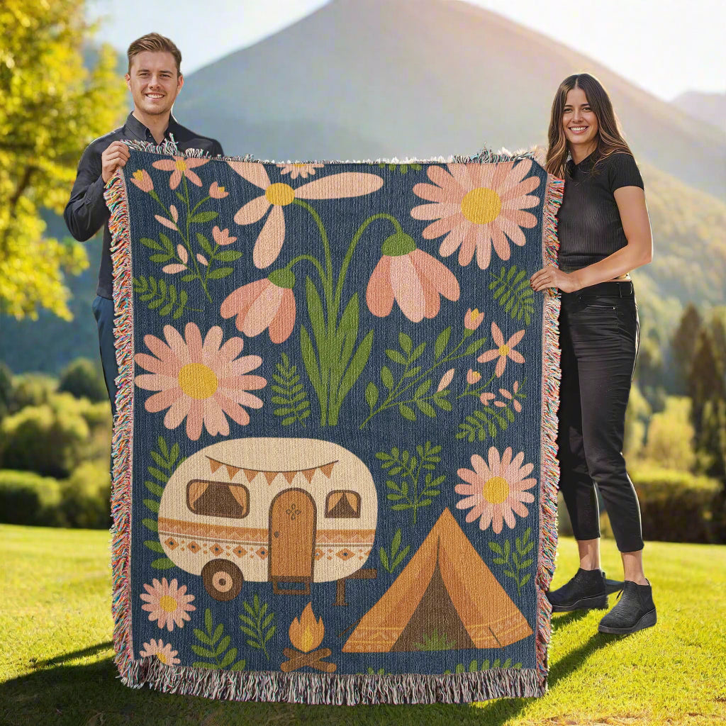 Two people holding a floral and camping-themed blanket outdoors.